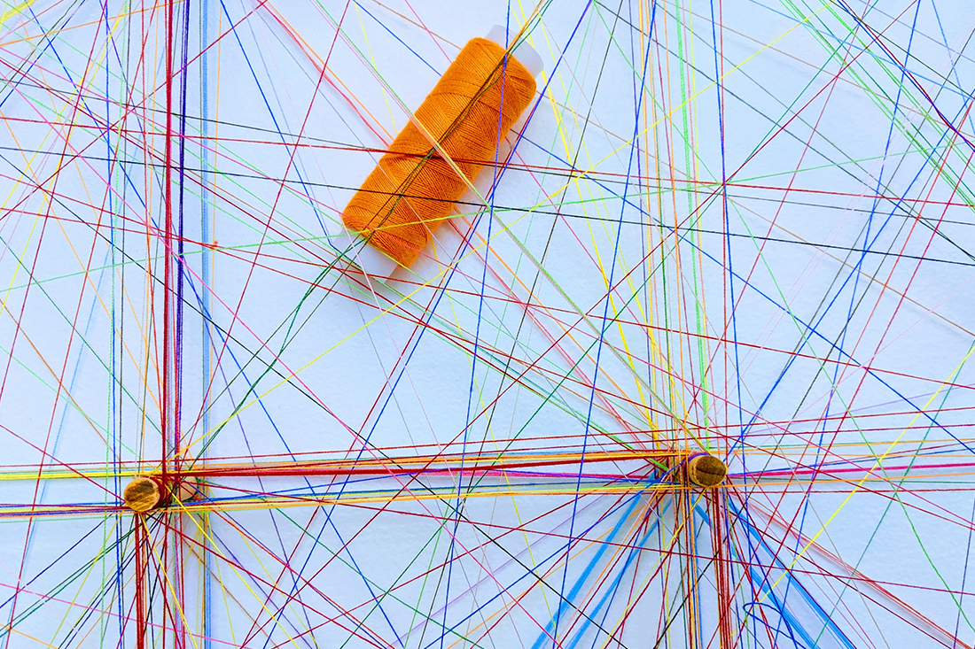 weiße Pinnwand mit verschiedenen farbigen Bindfäden und einer orangenen Garnrolle