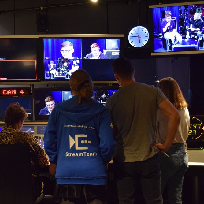 Bild zeigt vier Menschen vor großen Bildschirmen