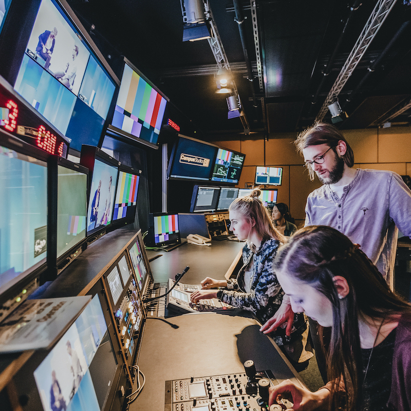 Bild zeigt 4 Personen vor einem langen Schreibtisch mit vielen Übertragungsbildschirmen.