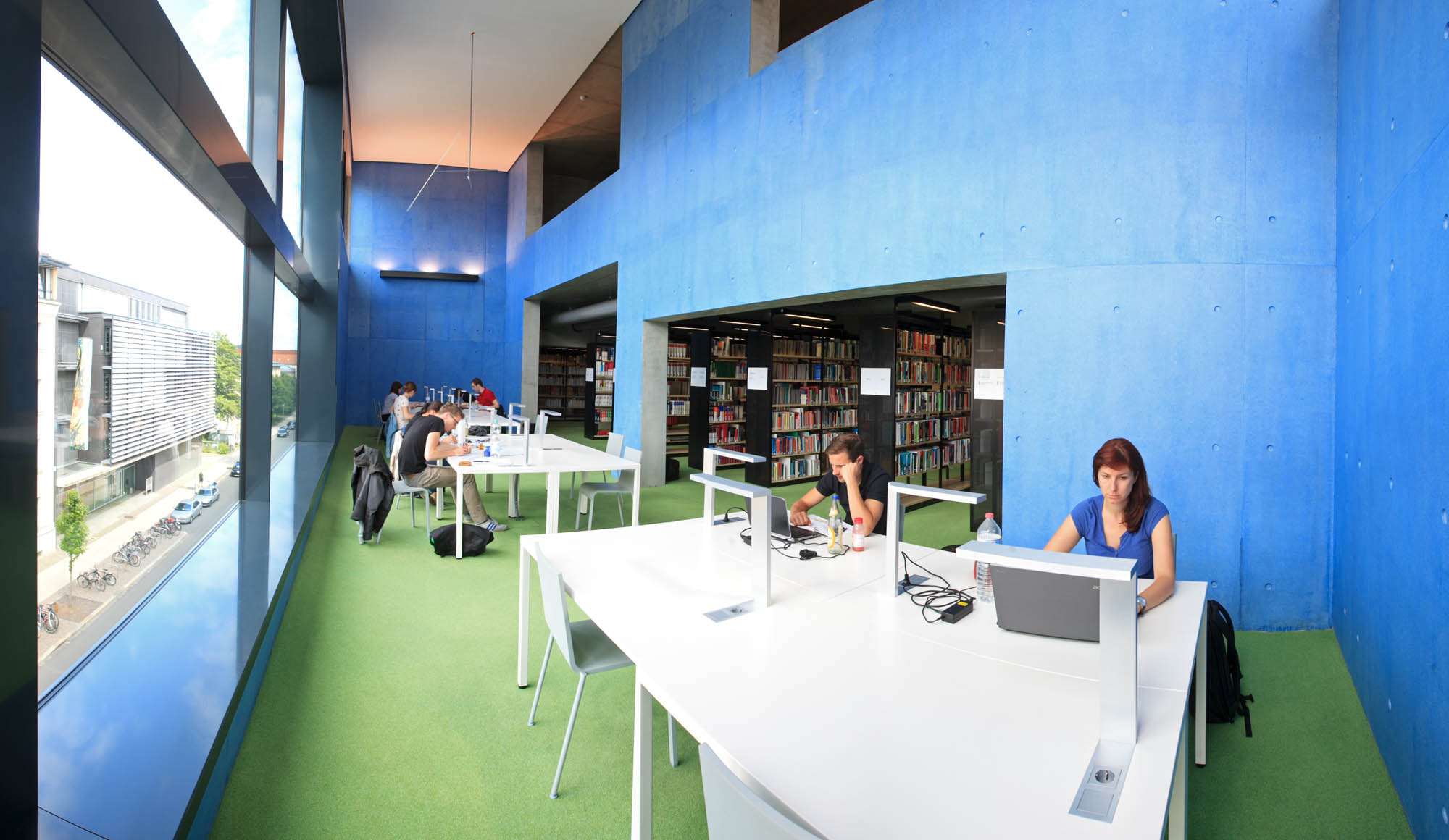 In der Hochschulbibliothek der HTWK Leipzig sitzen mehrere Studenten am Schreibtisch und arbeiten am Laoptop. Im Hintergrund sieht man Bücherregale.