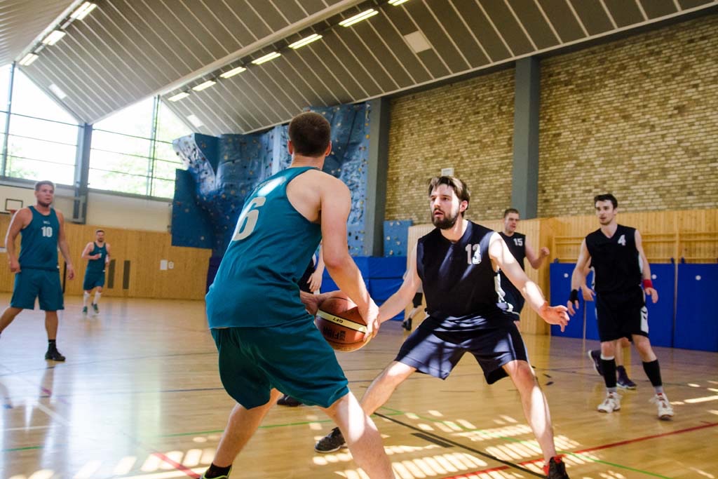 Mehrere Studenten spielen Basketball in einer Sporthalle. Zwei Spieler sind im Fokus.