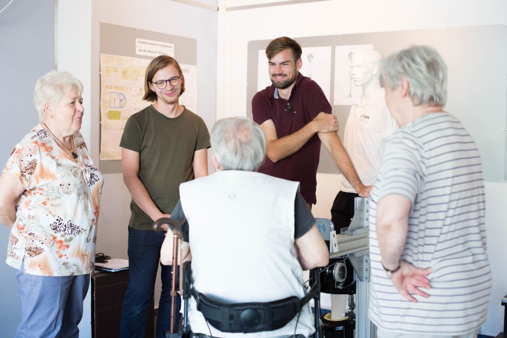 Im Sommer 2019 stellten die beiden Ingenieure ihr Exoskelett im Stadtteilladen Leipzig-Grünau aus. Dabei kamen sie mit potenziellen Anwenderinnen und Anwendern ins Gespräch (Foto: Lizette Ardelean/HTWK Leipzig). Präsentation, Exoskelett, Sommer 2019, Leipzig-Grünau